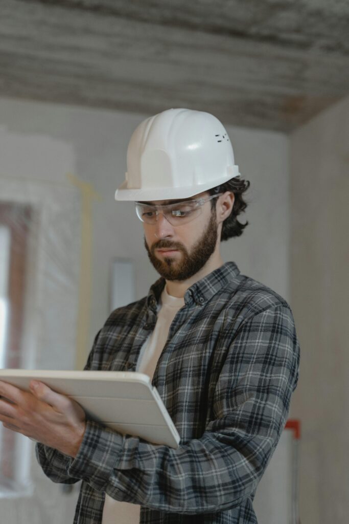 Male construction engineer assessing building plans indoors, wearing a hard hat.